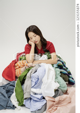 A woman in her 20s buried in a mountain of clothes. 123155874