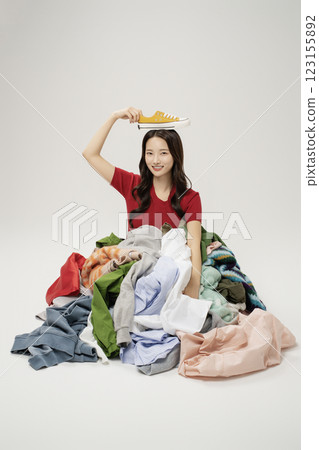 A woman in her 20s buried in a mountain of clothes. 123155892