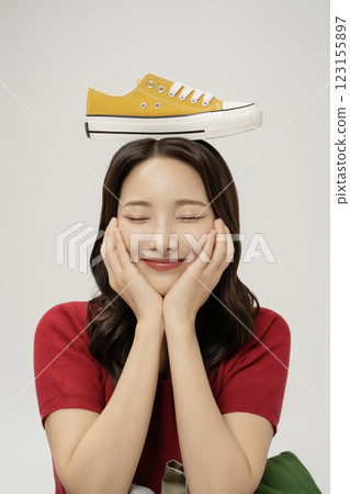 A woman in her 20s putting yellow sneakers on her head A woman in her 20s putting yellow sneakers on her head 123155897