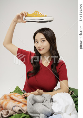 A woman in her 20s holding her shoes buried in a mountain of clothes. A woman in her 20s holding her shoes buried in a mountain of clothes. 123155899