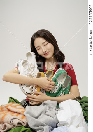 A woman in her 20s holding her shoes buried in a mountain of clothes. 123155902