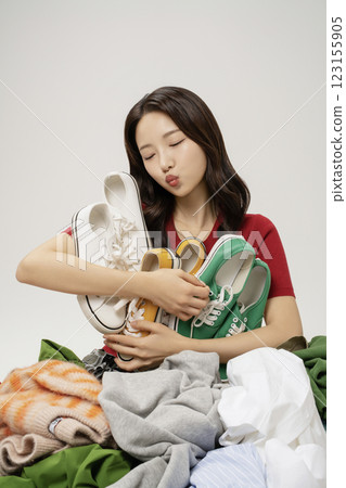 A woman in her 20s holding her shoes buried in a mountain of clothes. 123155905