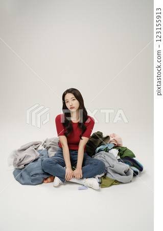 A woman in her 20s sitting in front of a pile of clothes 123155913