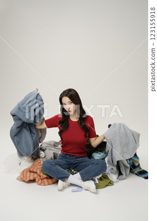 A woman in her 20s sitting in front of a pile of clothes 123155918