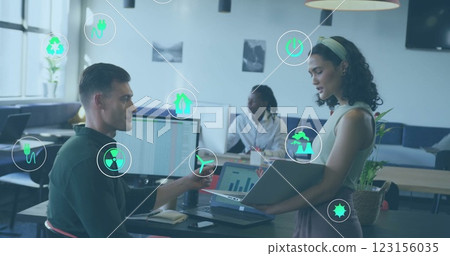 Image of ecology icons over diverse colleagues discussing work in office 123156035