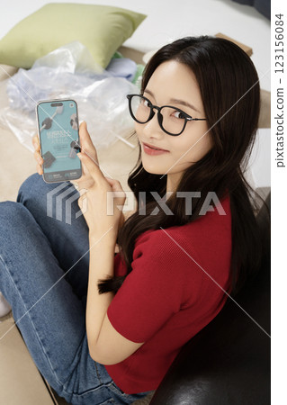 A young man in his 20s using his cell phone in a messy room 123156084