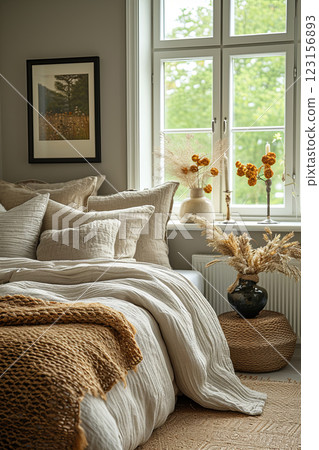 Cozy bedroom with a white bed and a window. The bed is covered with comforter and pillows. Vase with yellow flowers on a table 123156893