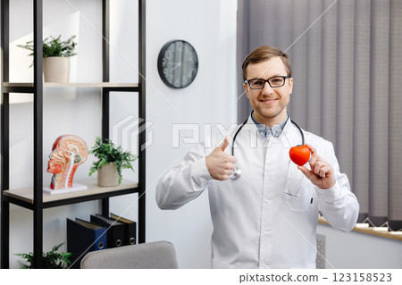 Doctor in white coat and glasses holding a red heart at hospital office. Medical health care and doctor staff service concept Doctor in white coat and glasses holding a red heart at hospital office. Medical health care and doctor staff service concept 123158523