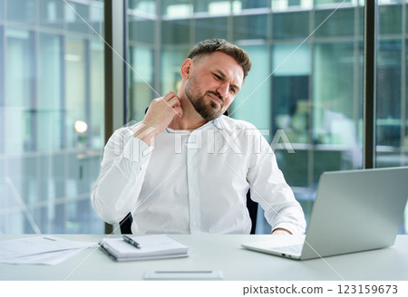 Professional Businessman in Office Experiencing Discomfort Working on Laptop 123159673