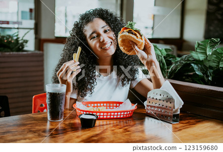 Afro young woman enjoying a hamburger with fries in a restaurant. Happy girl enjoying a hamburger in a restaurant 123159680