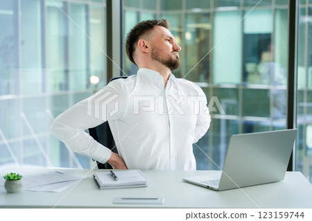 Office Worker Stretching Back While Seated at Desk with Laptop 123159744