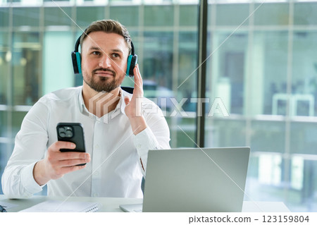 Professional Man Listening to Music With Headphones in Modern Office Setting 123159804
