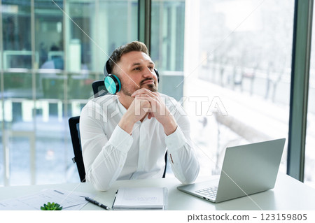 Professional Man Relaxing at Office Desk Listening to Music on Headphones 123159805