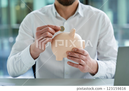 Businessman Adding Coin to Piggy Bank in a Professional Office Setting 123159816