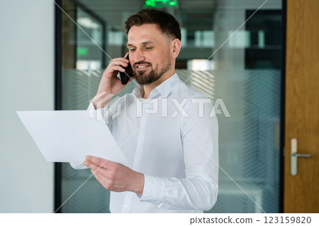 Professional Businessman Talking on the Phone and Reviewing Documents in Office 123159820