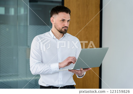 Confident Businessman Working on Laptop in Modern Office Setting Confident Businessman Working on Laptop in Modern Office Setting 123159826