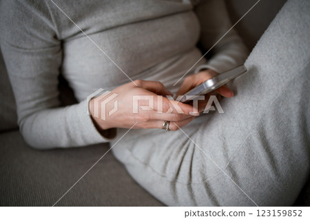Caucasian female adult using smartphone in casual gray outfit at home Caucasian female adult using smartphone in casual gray outfit at home 123159852