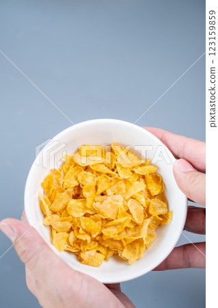 A white bowl filled with crispy golden cornflakes on a minimalist grey background. 123159859