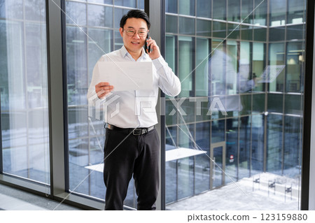 Professional Asian Businessman Discussing on Phone While Reviewing a Document 123159880