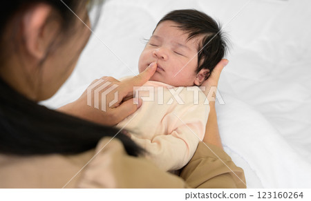 Mother touching mouth of newborn baby daughter on bed at home. Infant girl sleeping on mom arm. Love and new life concept 123160264