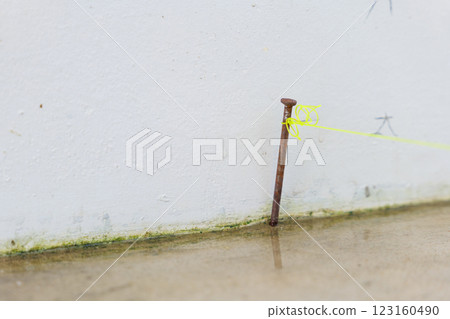 Precision in construction: a close-up of a nail hammered into concrete, intersected by yellow lines, emphasizing alignment in outdoor house tiling projects. 123160490