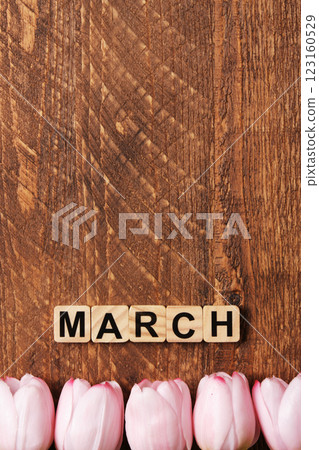 Word March in English made of wooden blocks with pink tulips on a brown wooden background. Space for your text. Word March in English made of wooden blocks with pink tulips on a brown wooden background. Space for your text. 123160529