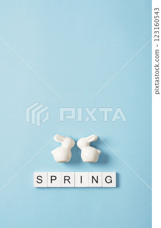 The word Spring in English on wooden blocks with white porcelain bunnies on a blue background. Space for your text. 123160543