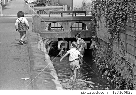 1970s: Black and white photo of Showa-era children playing in a waterway 123160923