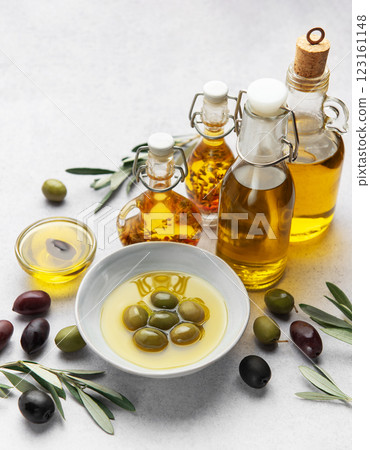 Bottles and bowls of golden olive oil with olives and olive branches residing on table Bottles and bowls of golden olive oil with olives and olive branches residing on table 123161148