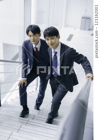 Portrait of two young businessmen standing on the stairs of an office building, vertical position Portrait of two young businessmen standing on the stairs of an office building, vertical position 123162001