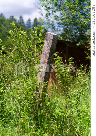 An old concrete post overgrown with grass and bushes. The remains of an abandoned and devastated garden fence. 123162298