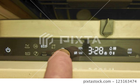 A male finger on the control panel of the dish washer. Switching programs on the dishwasher. Illuminated digital display buttons on the dishwasher. Closing the door of the built-in dishwasher 123163474