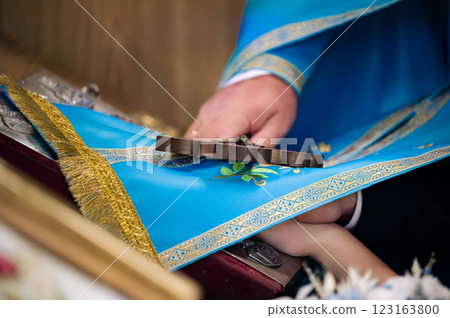 Close-up of hands holding a wooden cross during a religious ceremony. Blue liturgical cloth and gold embroidery are visible. Close-up of hands holding a wooden cross during a religious ceremony. Blue liturgical cloth and gold embroidery are visible. 123163800