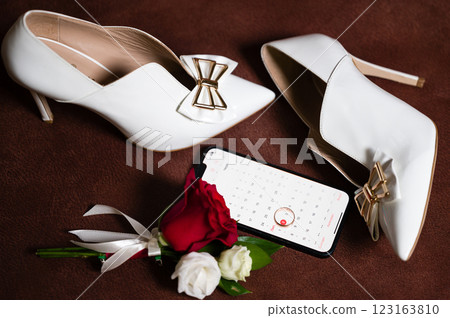 Elegant white heels, a calendar on a phone, and a boutonniere: wedding day details. Elegant white heels, a calendar on a phone, and a boutonniere: wedding day details. 123163810