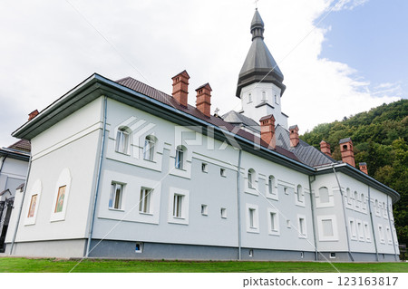 Modern monastery building with a tall tower and green hills in the background. 123163817