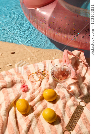 Sand with seashells, pink-striped towel, lemons, and rose drink, alongside gold accessories, celebrating elegance and relaxed summer vibe. Sand with seashells, pink-striped towel, lemons, and rose drink, alongside gold accessories, celebrating elegance and relaxed summer vibe. 123163831