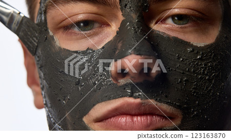 Close up of man's face, covered nourishment, skin care mask, his gaze directed forward against white studio background. 123163870