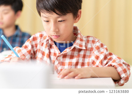 A male elementary school student writing with a serious expression A male elementary school student writing with a serious expression 123163880