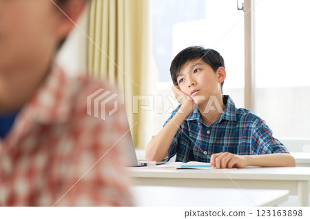 A boy in the upper grades of elementary school resting his chin on his hand and looking away A boy in the upper grades of elementary school resting his chin on his hand and looking away 123163898