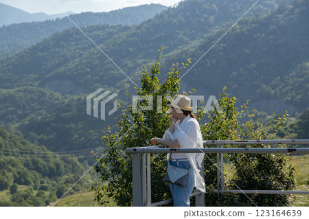Woman enjoying serene mountain views while standing on a lookout in the afternoon sun 123164639