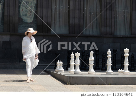 Elegant figure strolls through urban chess garden under the midday sun with unique giant pieces 123164641