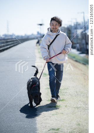 一名男子在河岸上遛一隻大狗 一名男子在河岸上遛一隻大狗 123165005