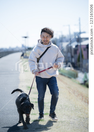 一名男子在河岸上遛一隻大狗 一名男子在河岸上遛一隻大狗 123165006