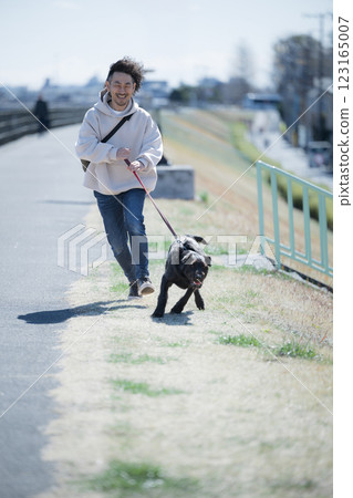 A man walking a large dog on the riverbank 123165007
