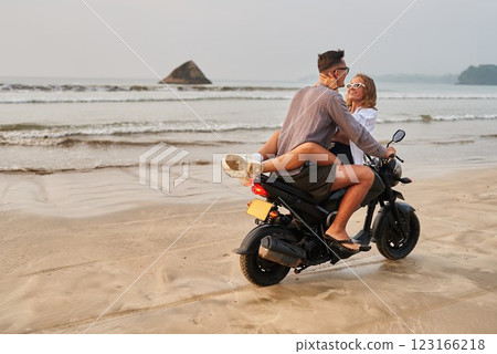 Young couple on beach motorbike. Lovers enjoy sand, sea riding motorcycle. Girl hugs guy on scooter, explore ocean shore romance, adventure. Man, woman on bike holiday. Young couple on beach motorbike. Lovers enjoy sand, sea riding motorcycle. Girl hugs guy on scooter, explore ocean shore romance, adventure. Man, woman on bike holiday. 123166218