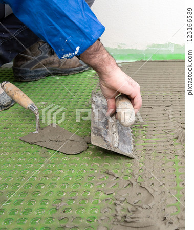 Tiler at work applies cement glue to the floor to install tiles. Construction. Tiler at work applies cement glue to the floor to install tiles. Construction. 123166589