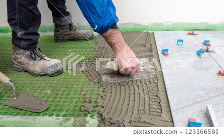 Tiler at work applies cement glue to the floor to install tiles. Construction. Tiler at work applies cement glue to the floor to install tiles. Construction. 123166591