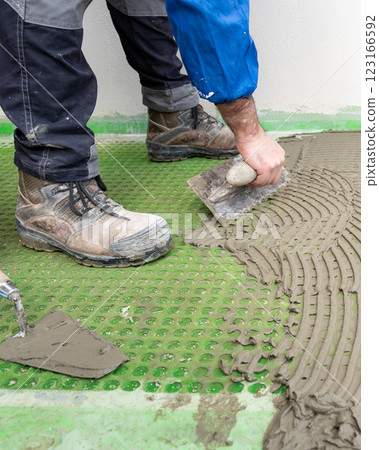 Tiler at work applies cement glue to the floor to install tiles. Construction. 123166592