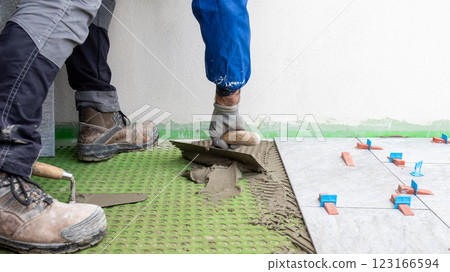 Tiler at work applies cement glue to the floor to install tiles. Construction. Tiler at work applies cement glue to the floor to install tiles. Construction. 123166594