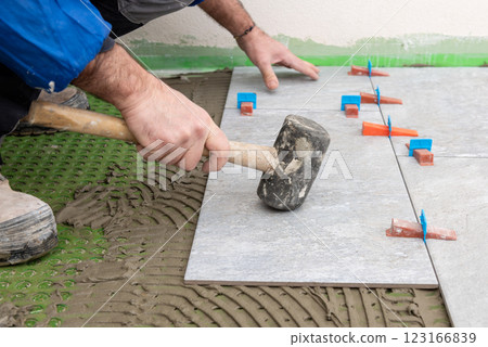 Tiler at work with rubber tile hammer. Construction. 123166839